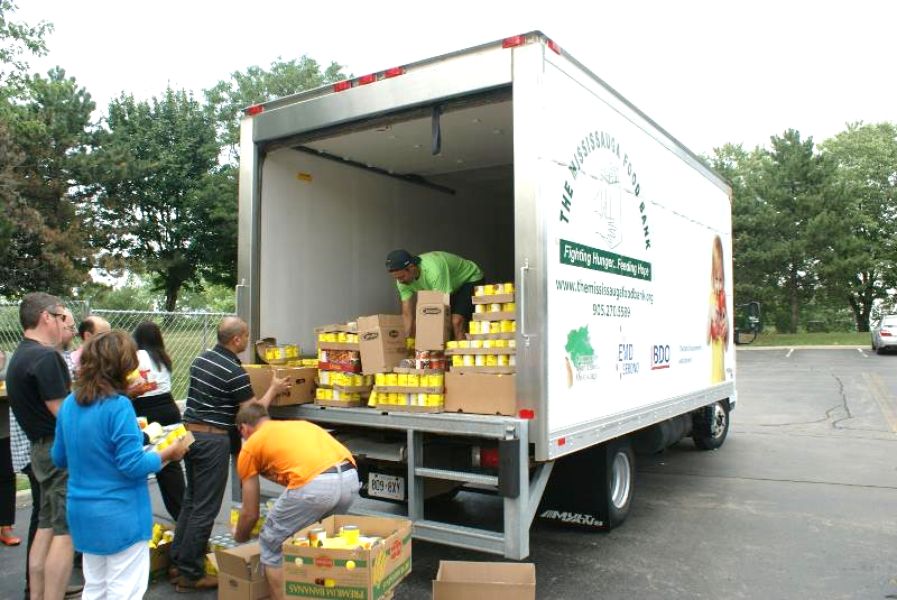 a large number of colleagues loading non perishable food items into a truck to be donated to charity as a result of their charitable team building activity