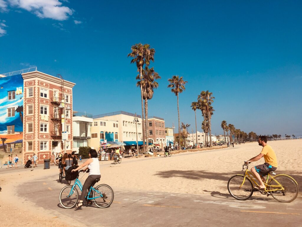 People cycling and walking down sunny Venice beach boardwalk.