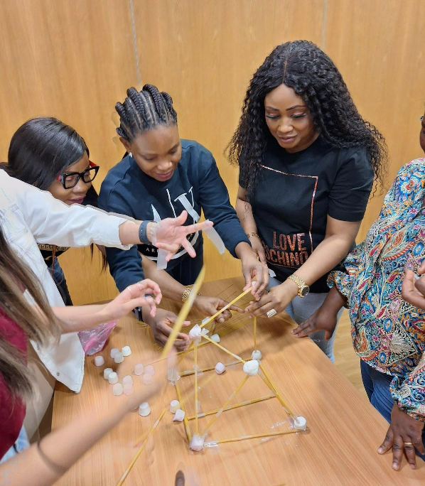  people gathered around table making a marshmallow tower