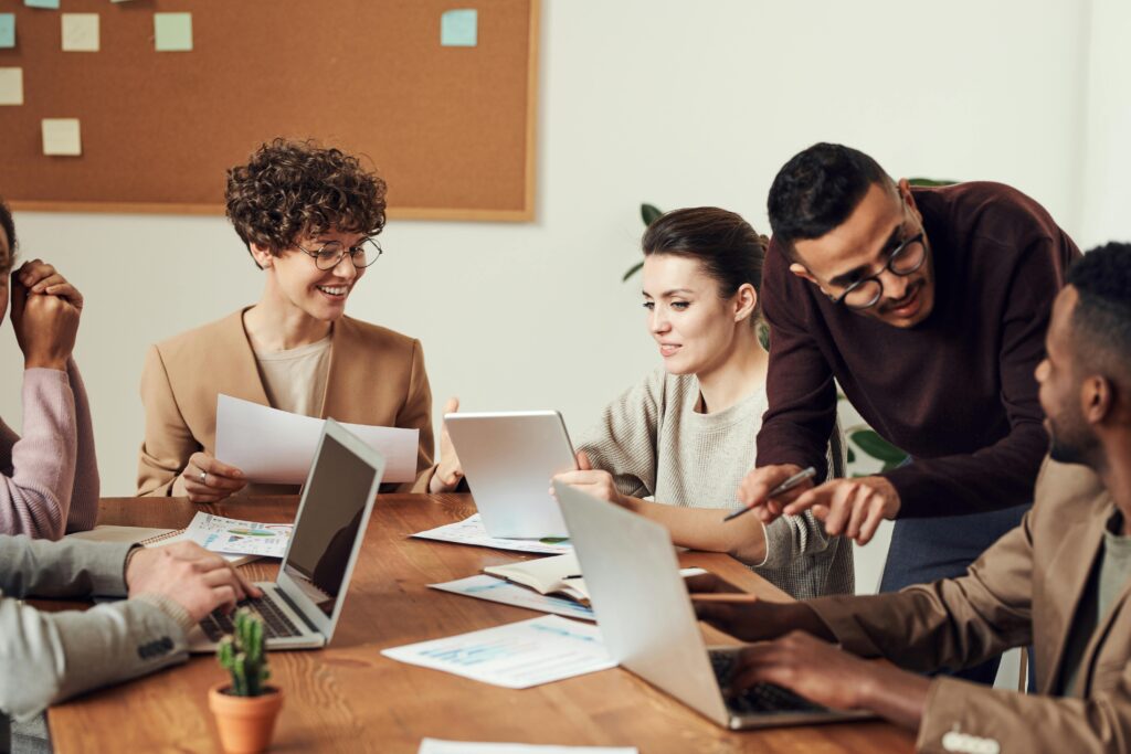 group of people sitting at table with their laptops discussing work